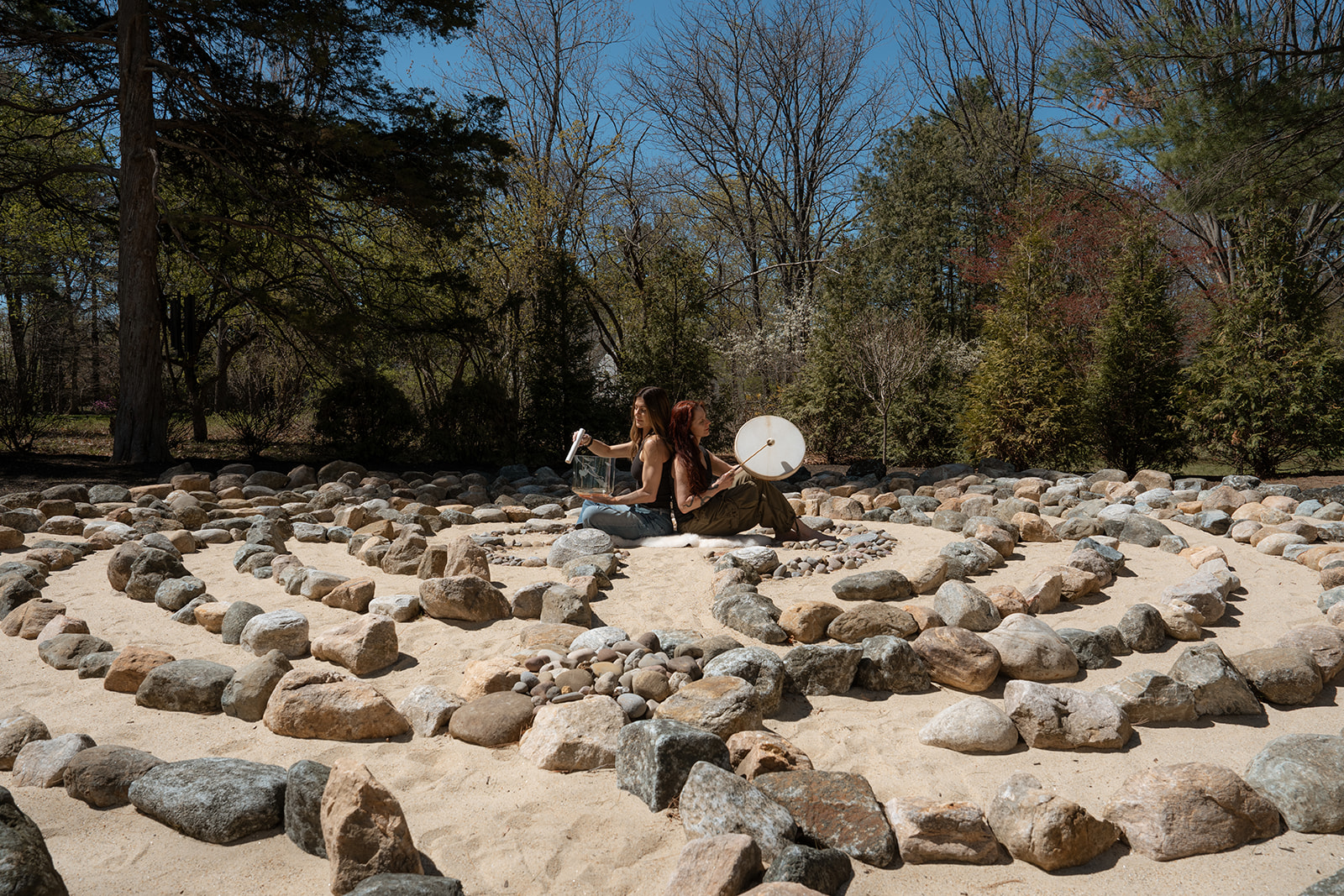Christine Grace and Melinda Pavlata sitting back-to-back at the center of a stone labyrinth.
