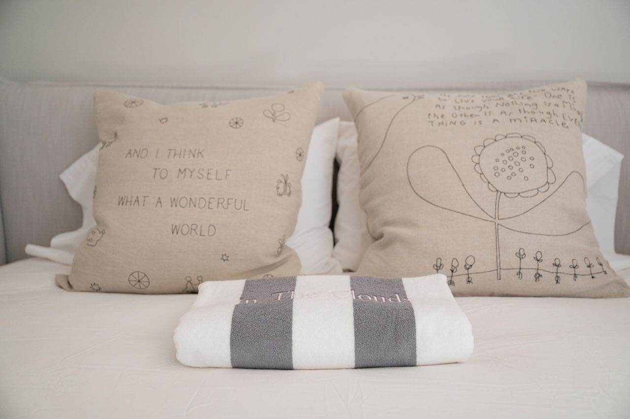 A guest bed with hand-stitched pillows reading 'what a wonderful world' and folded towels.