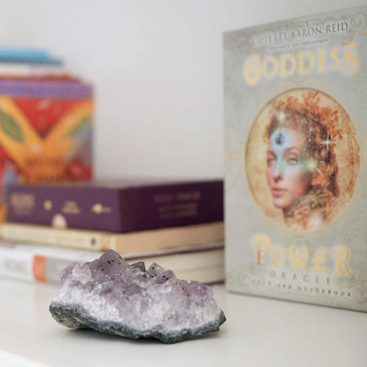 An amethyst cluster next to a stack of oracle decks and books on a bedside table.